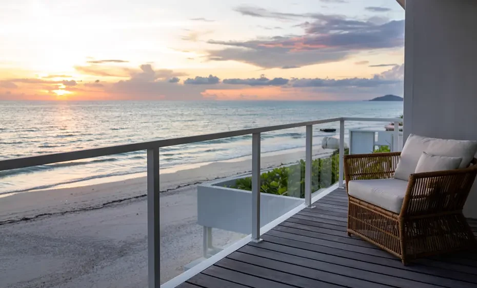 A tropical hotel balcony in Thailand overlooking the ocean, empty, discreet, with warm sunset lighting.