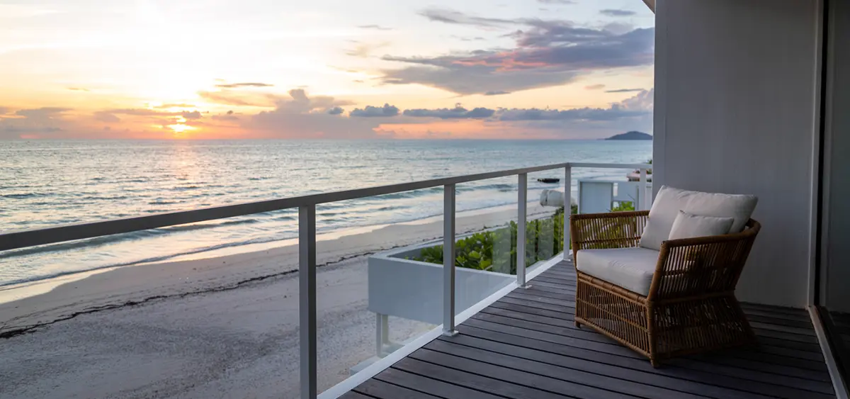 A tropical hotel balcony in Thailand overlooking the ocean, empty, discreet, with warm sunset lighting.