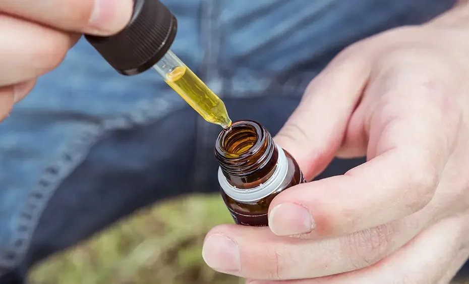 A person holding a dropper bottle of CBD oil, demonstrating legal cannabidiol use in Thailand.