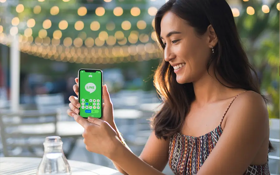 Thai woman using the LINE messaging app on her smartphone, ideal for private cannabis promotions.